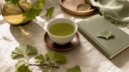 Ruhige Schreibtischszene mit Grüntee und Ginkgo-Blättern auf hellem Leinen im weichen Tageslicht.